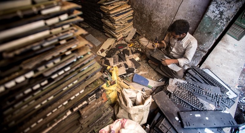 Man works on electronic repairs among giant stacks of components.