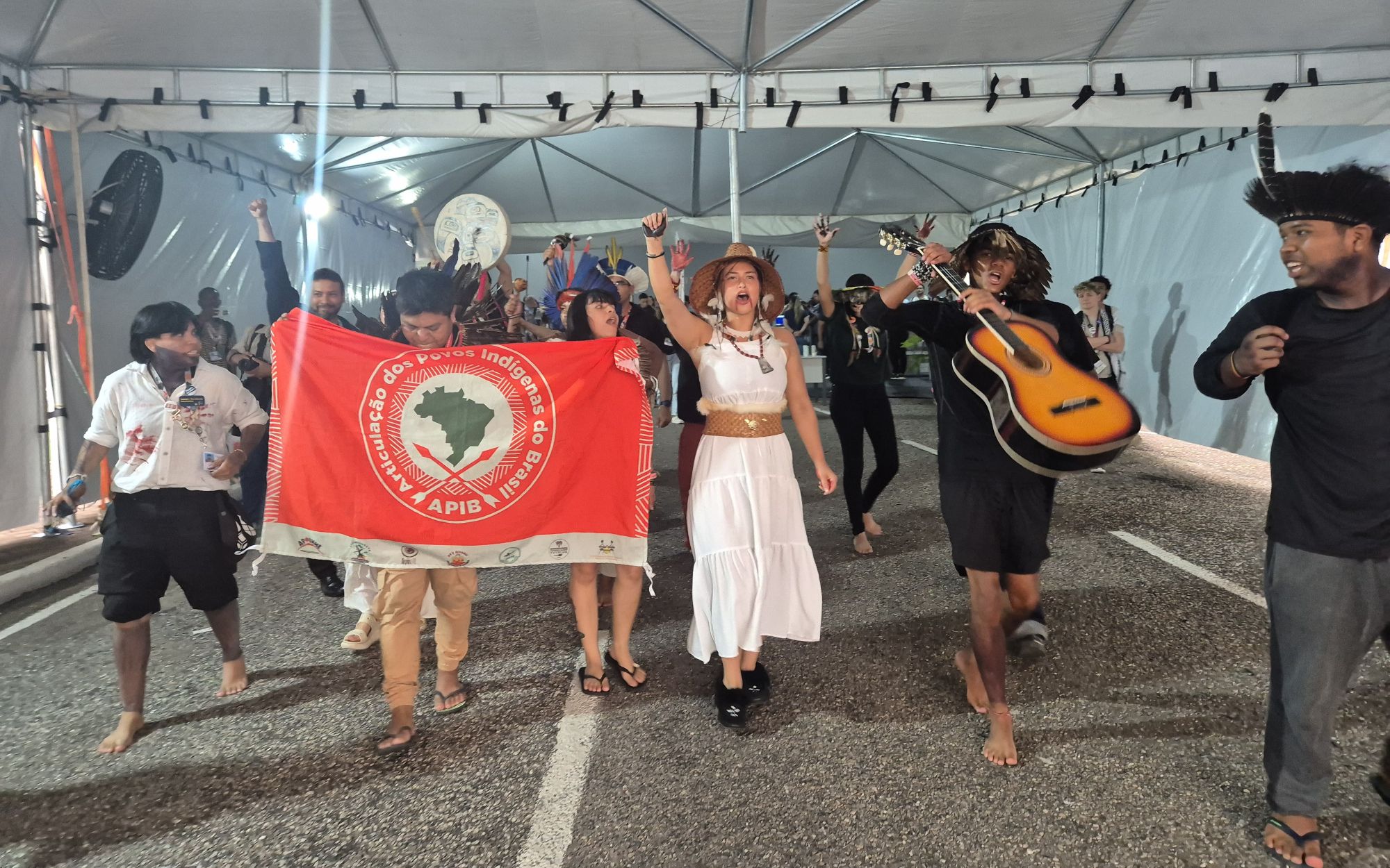 Grupo de personas marchando con una bandera roja y un hombre llevando una guitarra