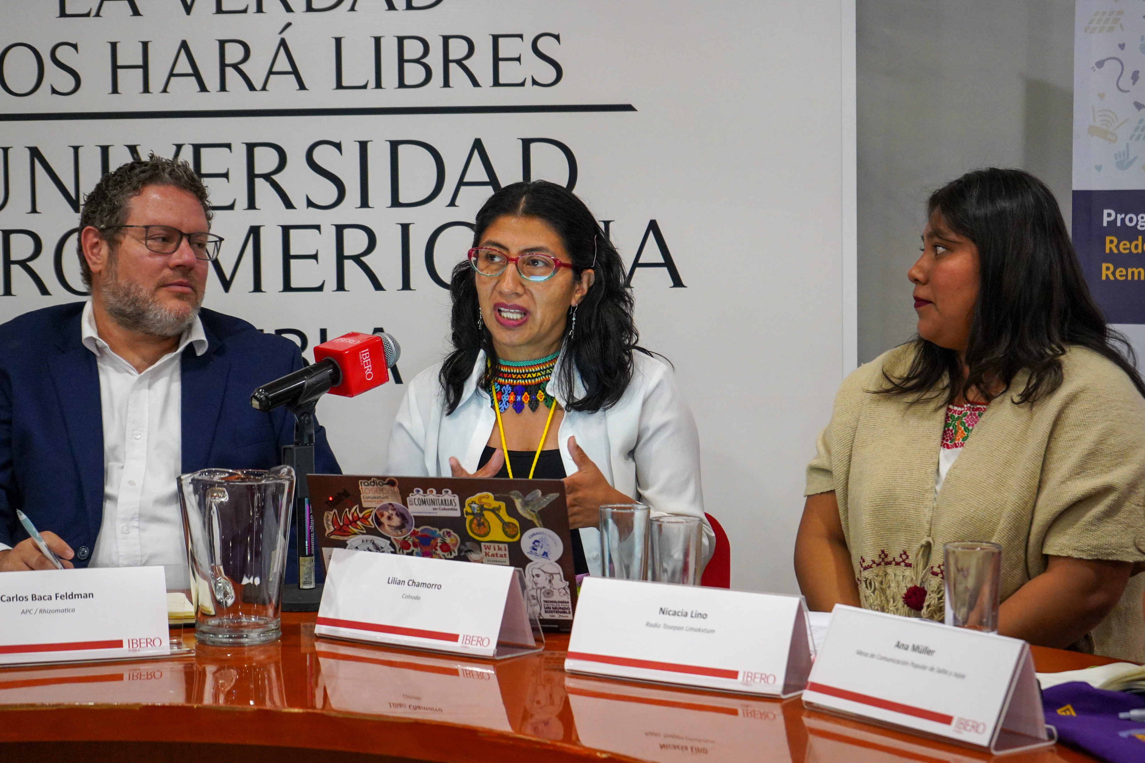 Three persons in a table, the women in the center is talking with a microphone.