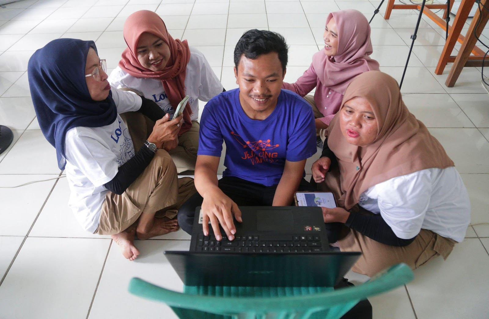 A group of people, a man and four women, sitting on the floor working around a notebook
