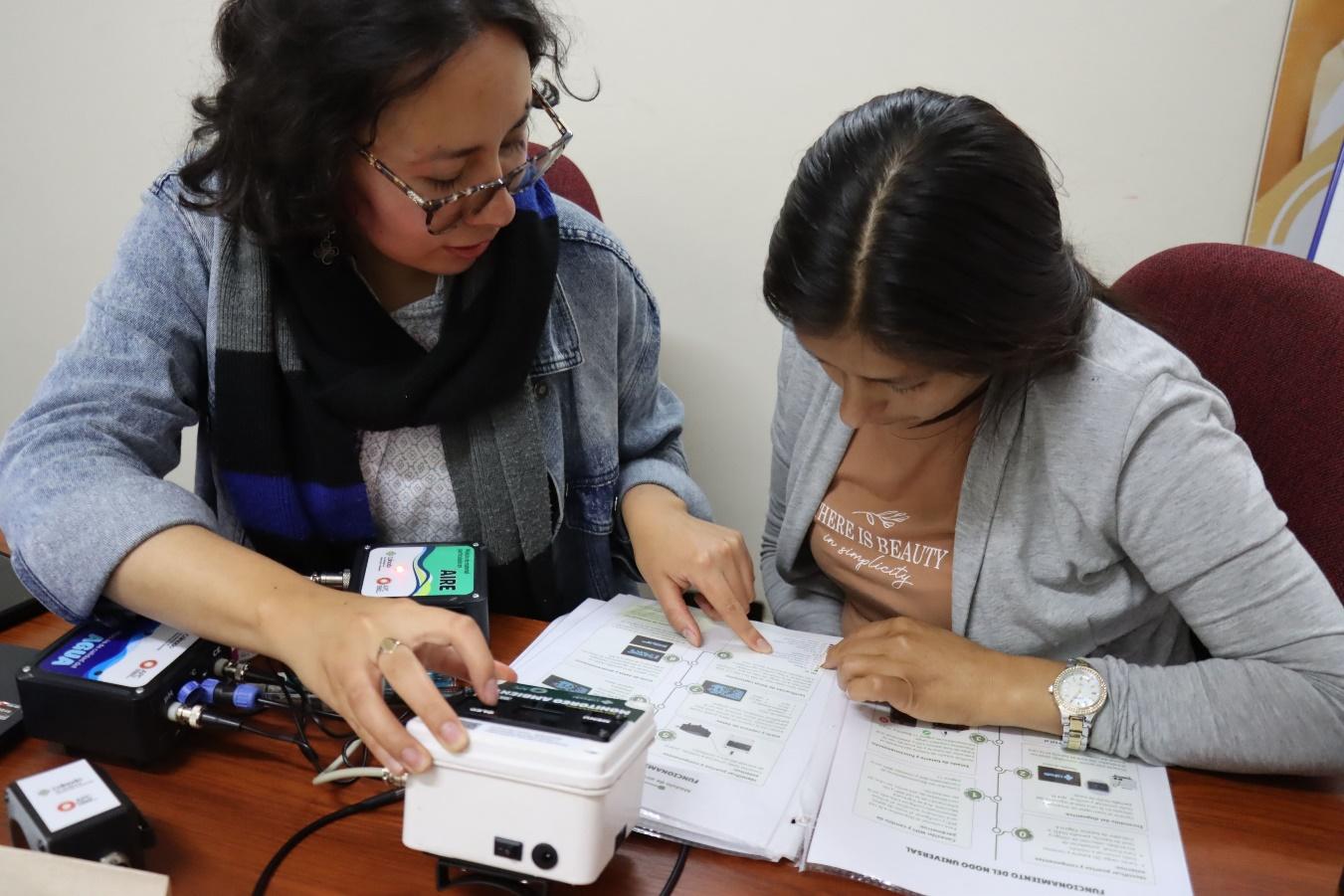 "Two women review documents and monitoring equipment during a training session."