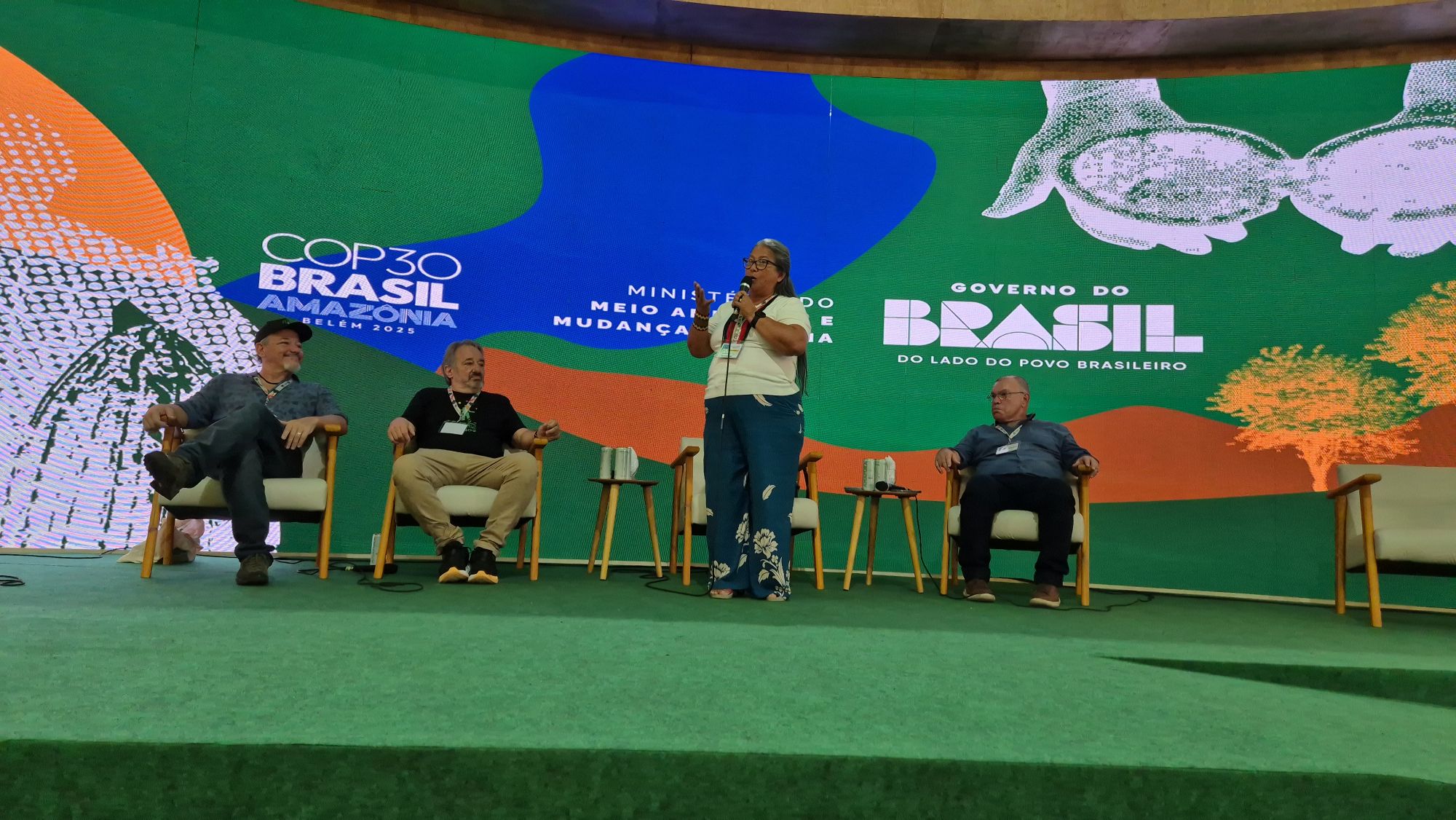 una mujer hablando en una panel con fondo verde