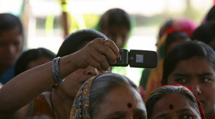 Photo: Woman takes photo with cellphone at a community meeting. Simone D. McCourtie/World Bank via Flickr