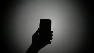 Silhouette of a hand holding a mobile phone image linking to Waging war on digital feeds: How platforms and governments fuel violence at the virtual frontline 