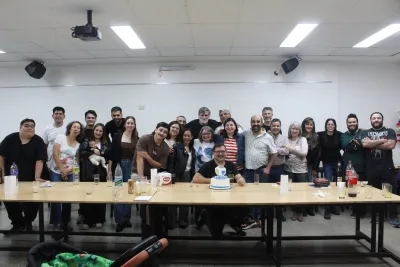 Un grupo diverso de personas reunidas en un aula, sonriendo alrededor de una mesa con una torta decorada. image linking to 30 años acercando herramientas digitales a los sectores populares en Argentina 